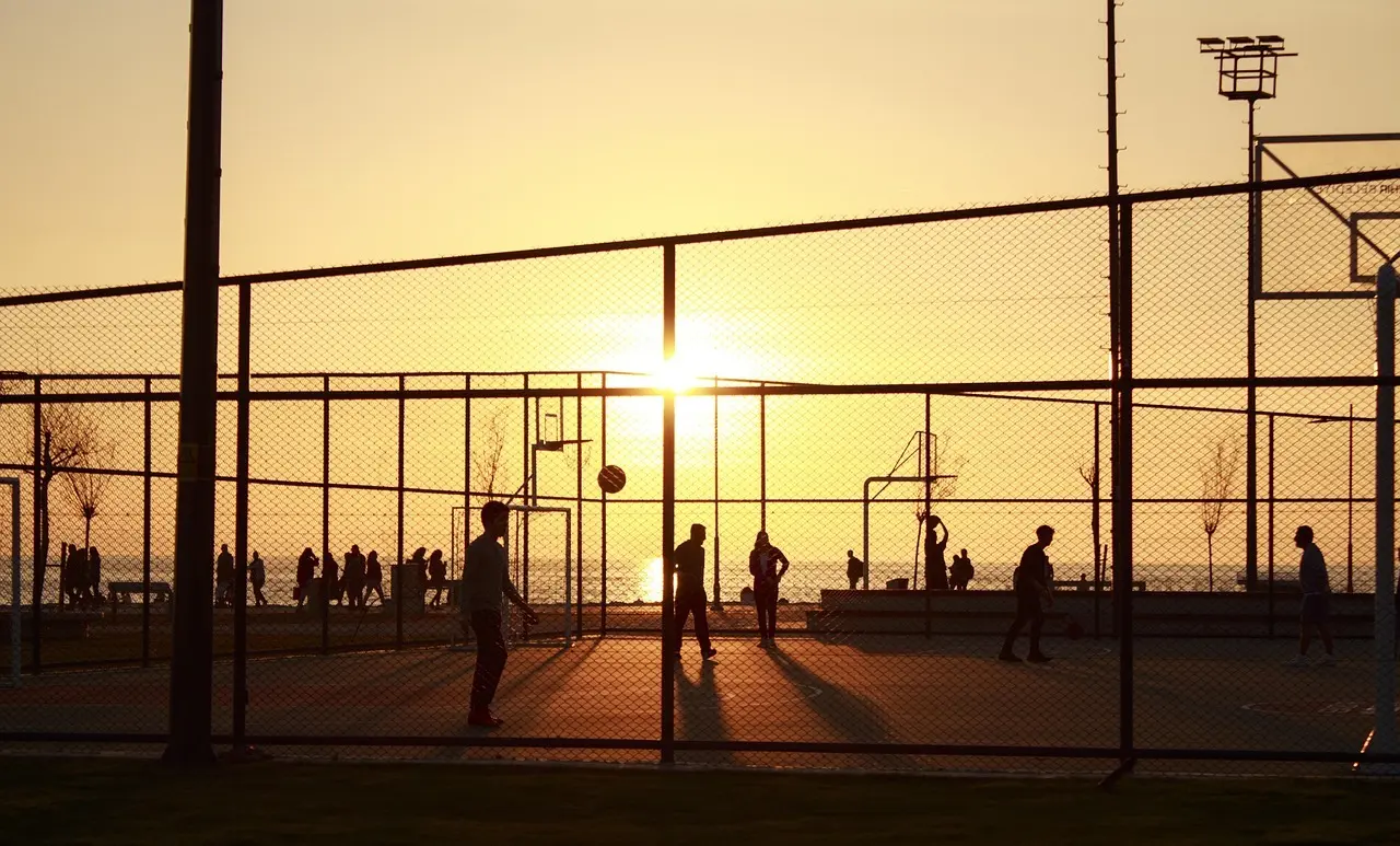 Personer der spiller basketball ved solnedgang